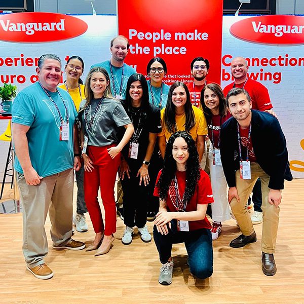 Group of employees posing together at a Vanguard event booth with red signage that reads “People make the place,” standing in front of a branded display with additional messaging about connections and career opportunities.
