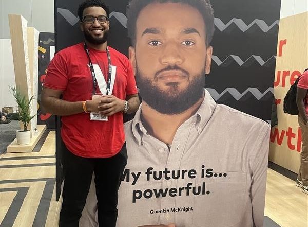 Quentin standing in front of AfroTech booth that features a photo of himself