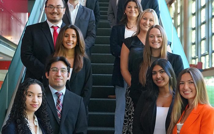 Cohort of crew in a Vanguard specialty program, dressed in business attire and standing on an indoor staircase with glass panels and large windows in the background.