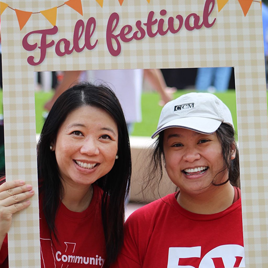 Two people smiling while holding a Fall Festival photo frame during a Community 365 event on a grassy campus area in Arizona
