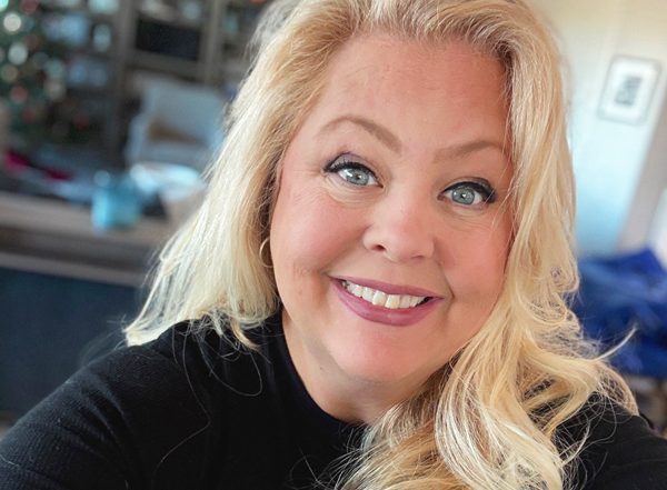 Tracy L. smiling confidently in a black top, photographed indoors, facing the camera in a home setting with a softly blurred background.