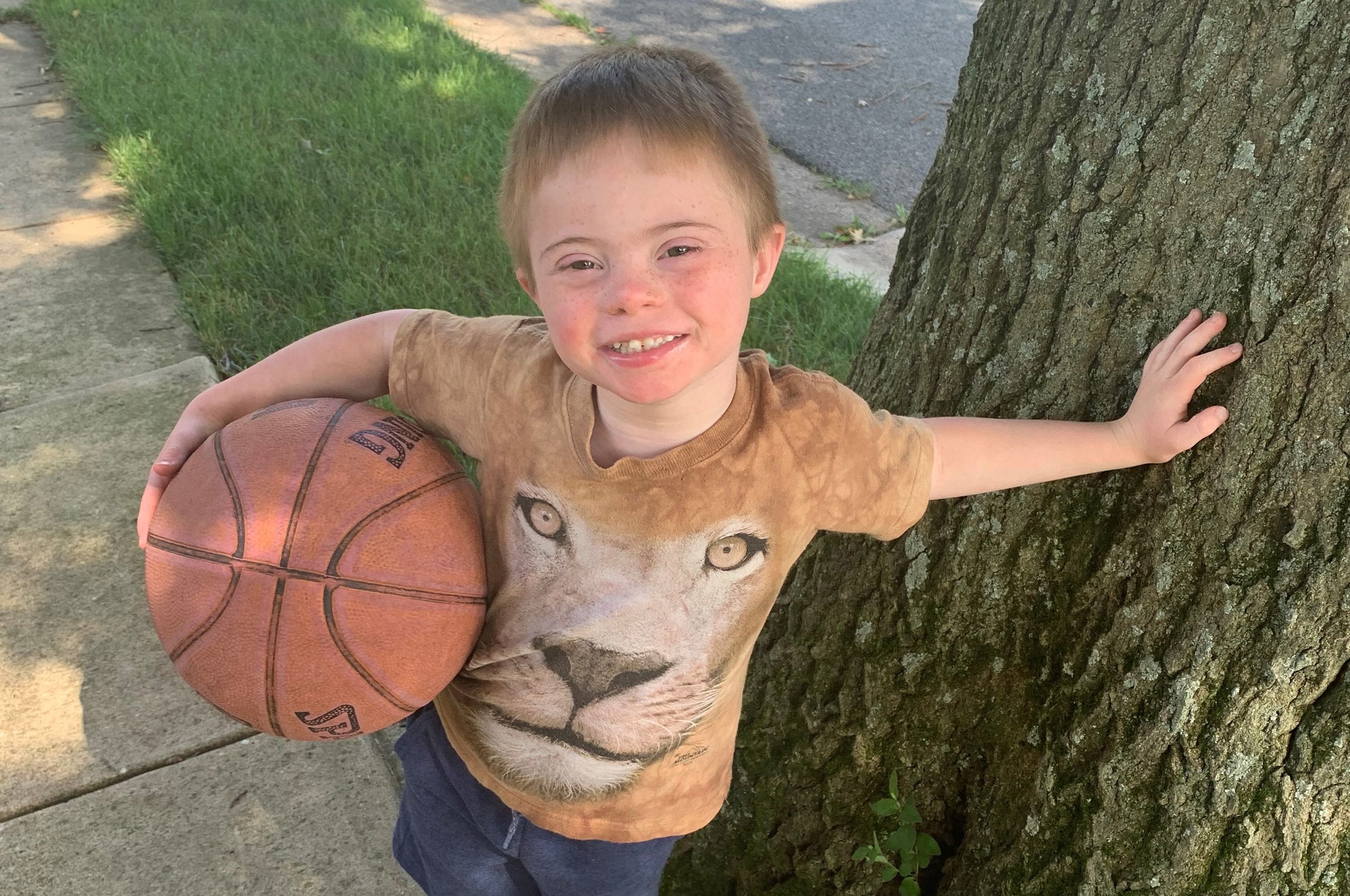 Ted G.'s son Nate outside standing next to a tree while holding a basketball.