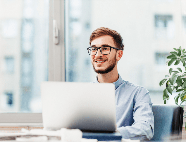 A young man with a laptop, gazing into the distance and smiling. 