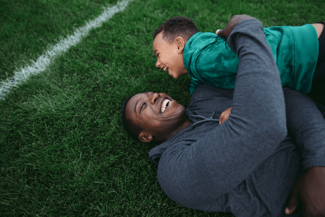 Father and son laying on football field, laughing, after a tackle.