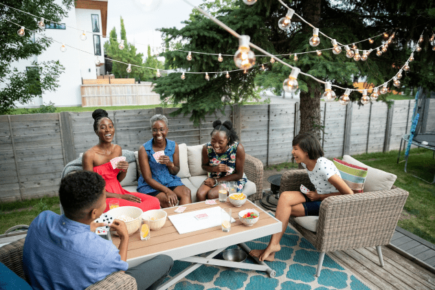 A group of family and friends of varying ages playing card games and laughing together in a backyard.