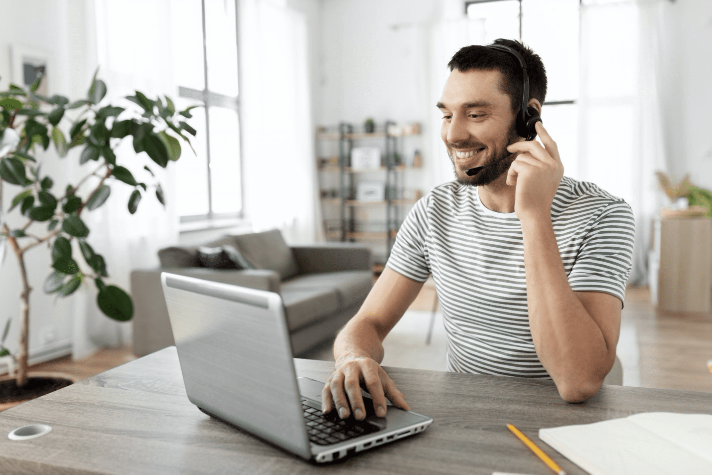 employee sitting at home workspace wearing a headset and engaging with clients on laptop
