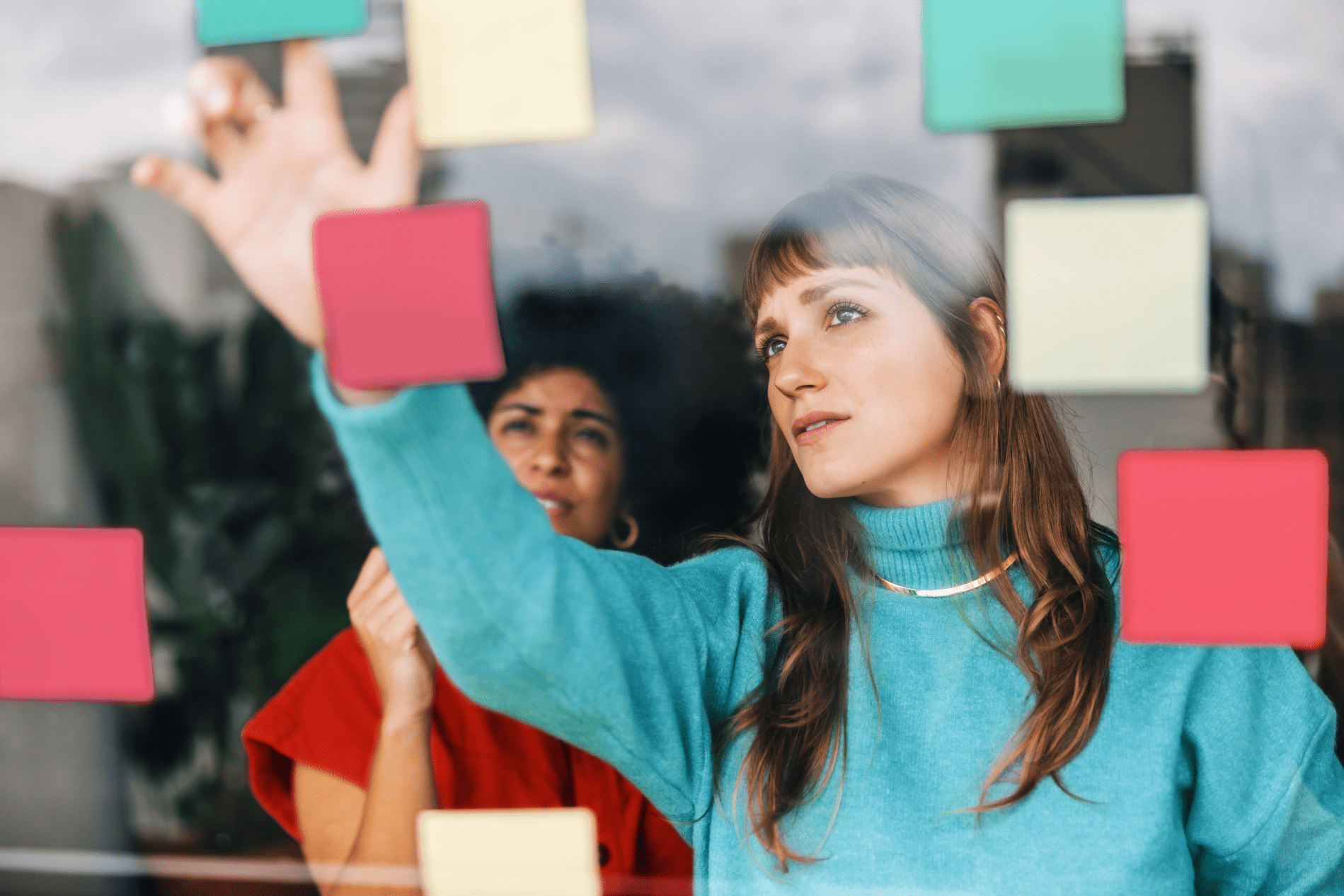 Two coworkers evaluating a wall of multicolored sticky notes together.
