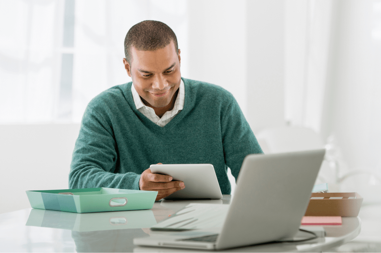 A man sits at a table and looks at the tablet he is holding.