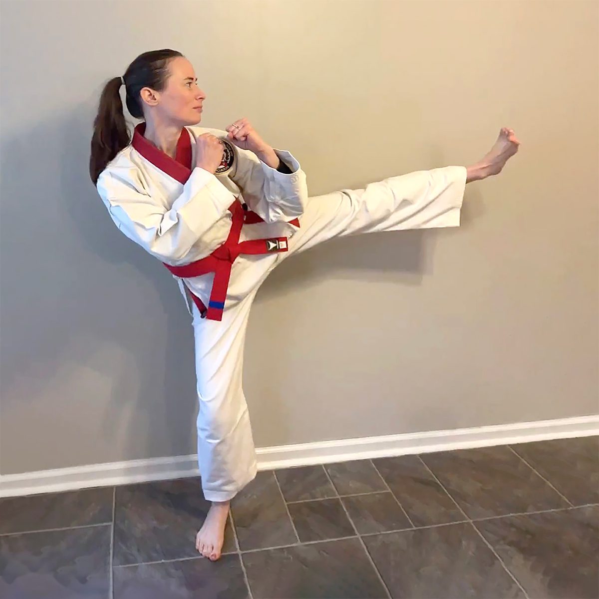 Jill in a karate uniform is in a stanced position, kicking her right leg forward.