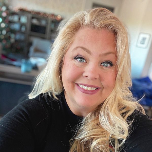 Tracy L. smiling confidently in a black top, photographed indoors, facing the camera in a home setting with a softly blurred background.