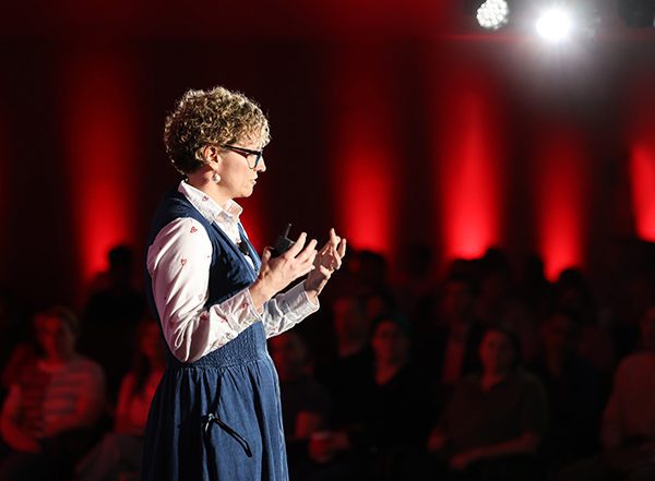 Crew presenter on stage at the unlimITed conference, with dramatic lighting featuring spotlights and red perimeter lighting.